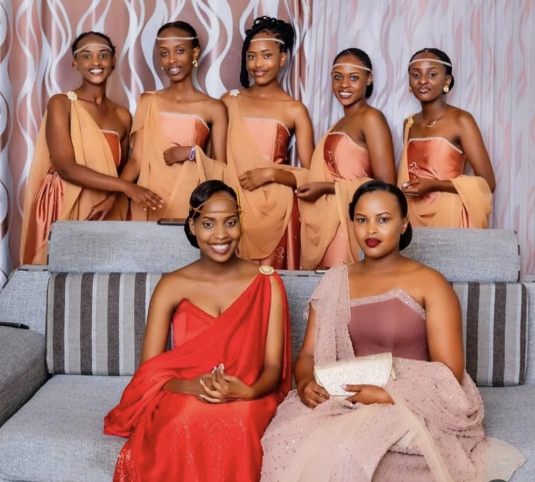 A Rwandan bride seated with her bridal party, all wearing mushanana in coral, peach and blush.